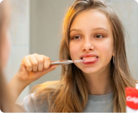 Menina escovando os dentes em frente a um espelho como parte de uma rotina saudável de higiene bucal.
