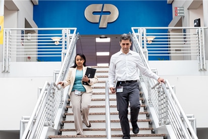 Funcionários da Colgate-Palmolive descendo uma escada, com o logotipo da Colgate-Palmolive ao fundo em uma parede azul.