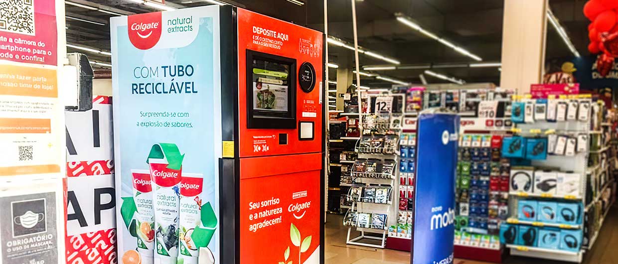 Totem interativo de reciclagem da Colgate com anúncio de tubo reciclável instalado no corredor de um supermercado.